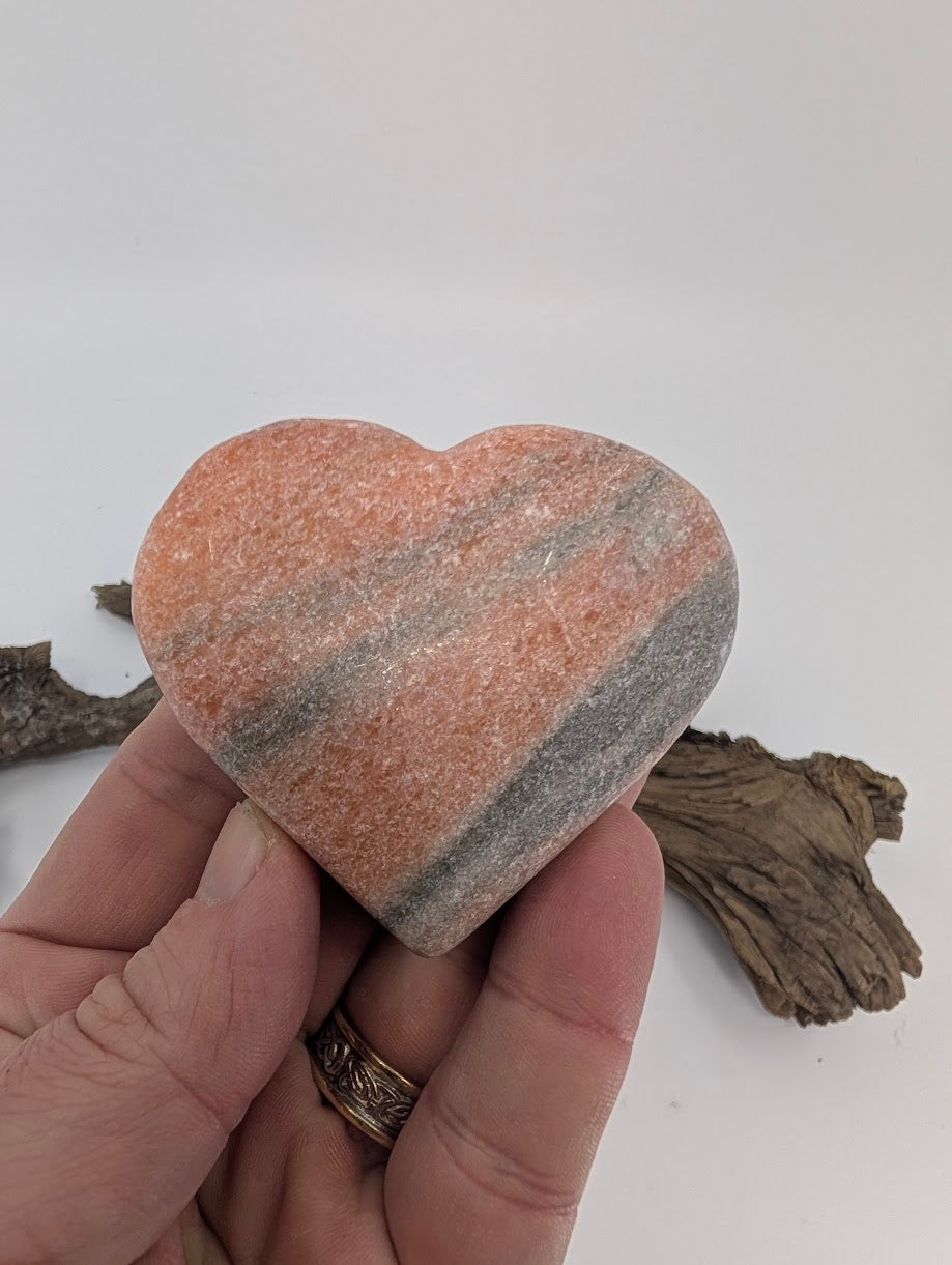 Hand holding a 150g Sunstone heart showing peach color and grey striations.