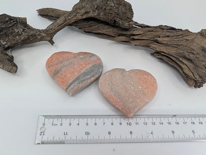 Two polished Peach Sunstone hearts displayed on driftwood.