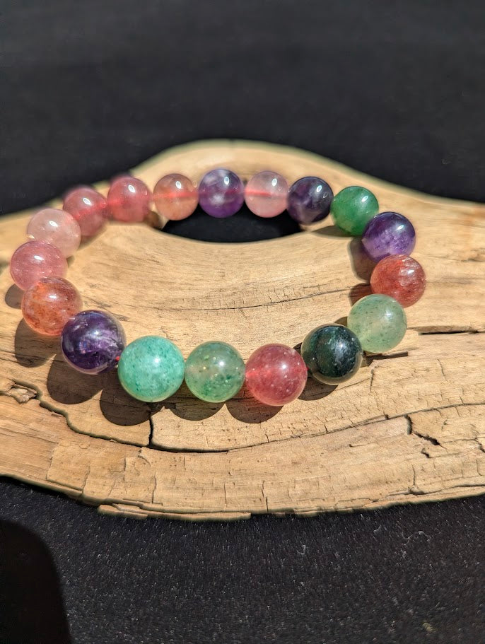 11mm Super 8 mixed quartz beaded stretch bracelet resting on a driftwood display, showing multi-coloured purple, green, and red stones strung on a pink elastic cord.