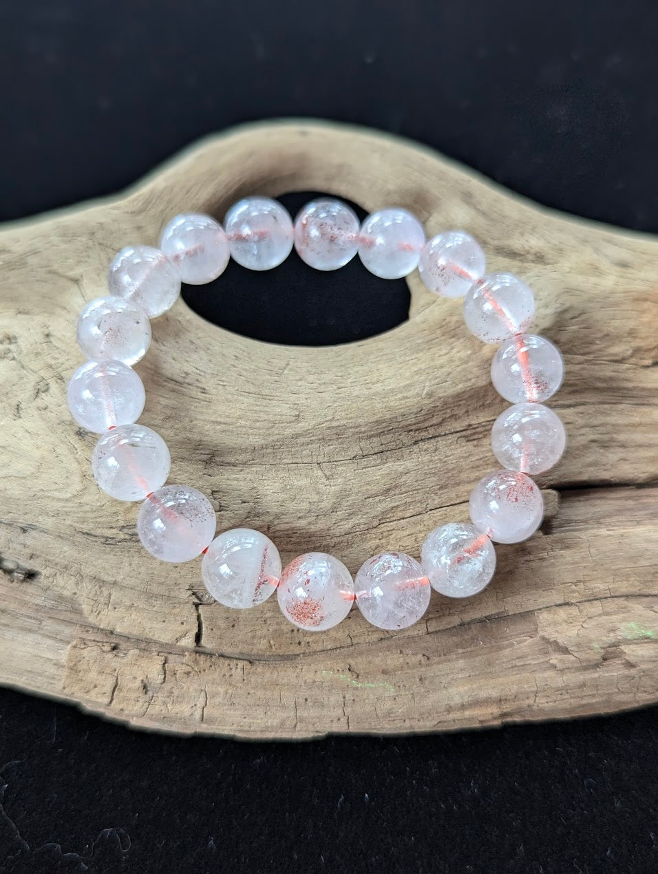 Substantial 11mm AA Grade Super Seven gemstone bracelet resting on rustic wood, maximizing the display of clear quartz and red lepidocrocite.