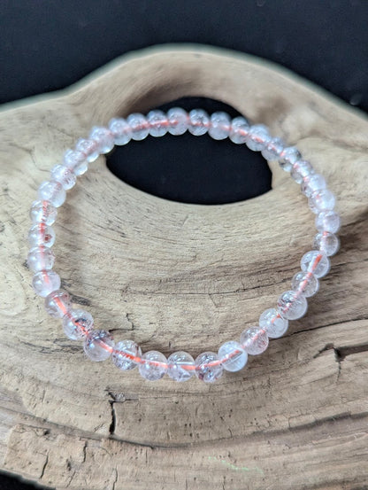 5mm AA Grade Super Seven gemstone bracelet from the Congo resting on natural driftwood, showcasing clear quartz with red lepidocrocite inclusions.