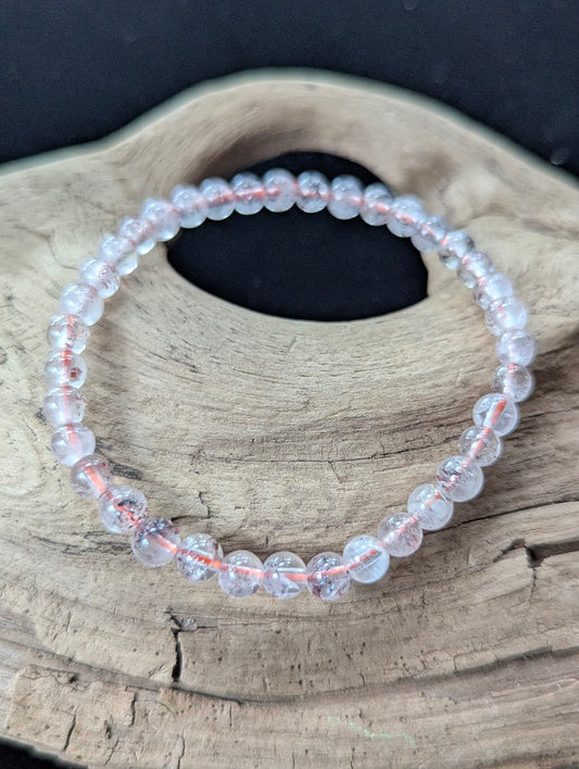 5mm AA Grade Super Seven gemstone bracelet from the Congo resting on natural driftwood, showcasing clear quartz with red lepidocrocite inclusions.