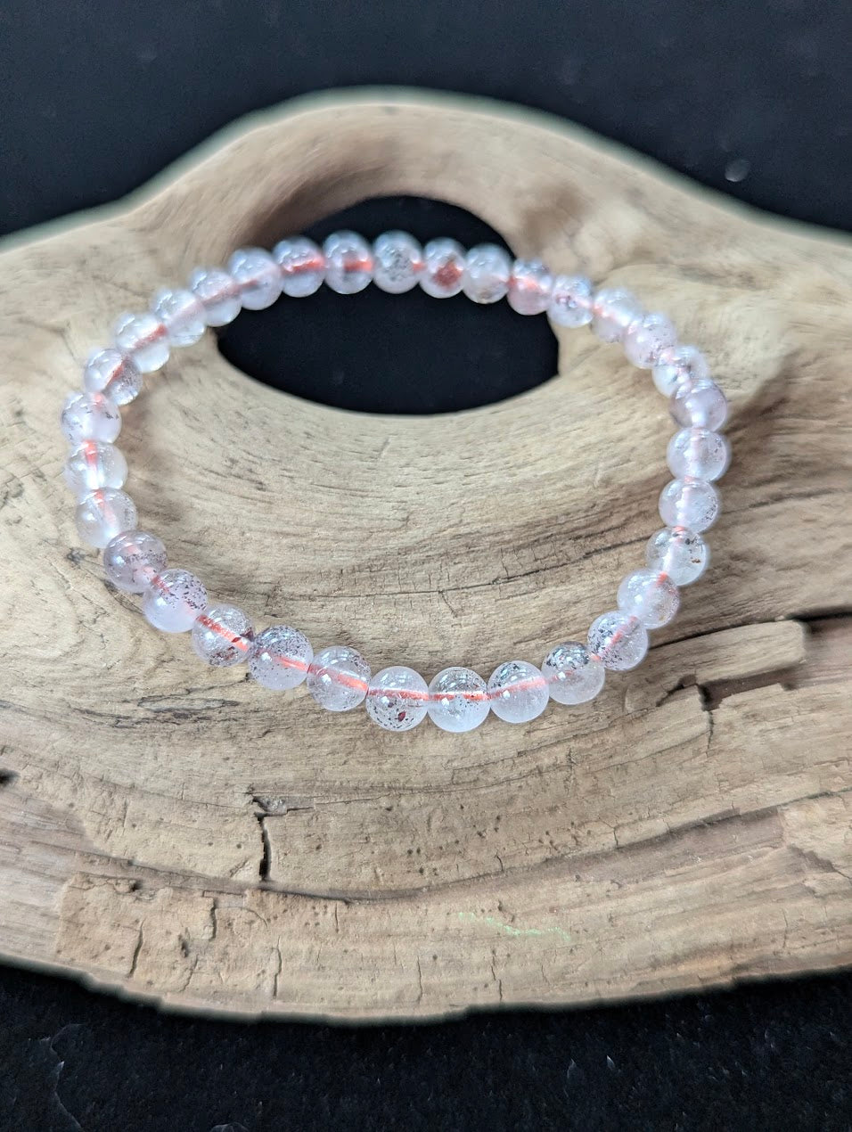 6mm AA Grade Super Seven beaded bracelet displayed on textured wood, revealing beautiful red hematoid flakes within clear quartz.