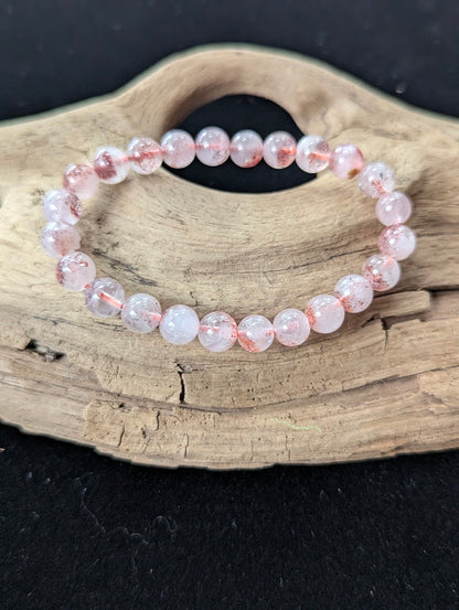 7mm Super Seven bracelet displayed on natural driftwood, showing glassy bead clarity and striking orange-red internal minerals.