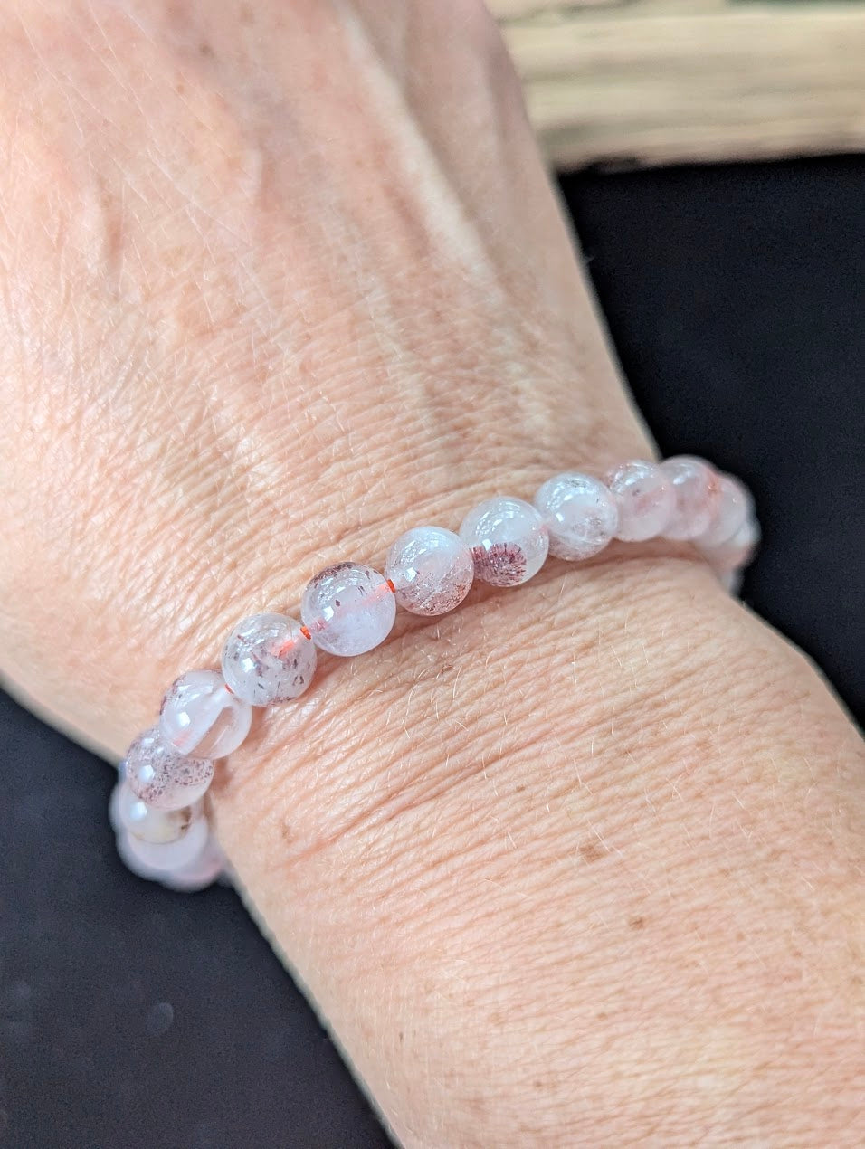 7mm Super Seven beaded bracelet worn on a wrist, catching the light to highlight its inner red mineral structure.