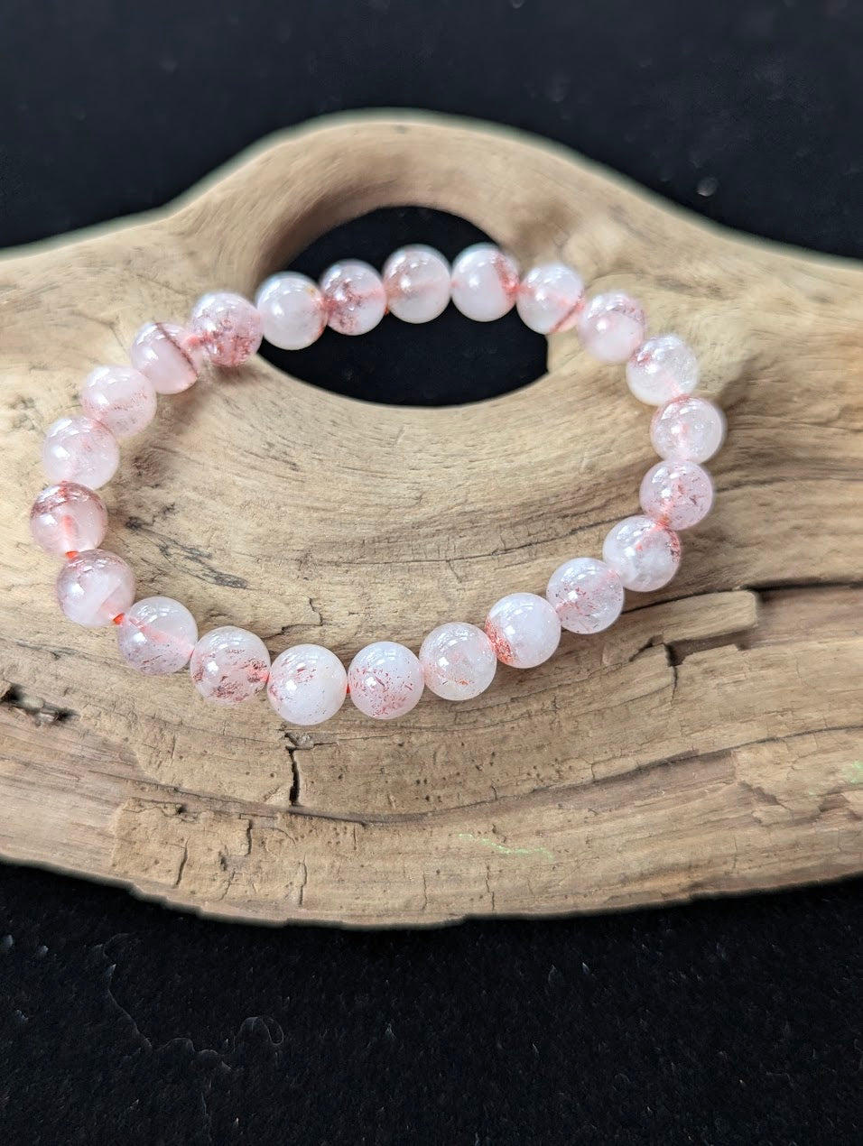 8mm AA Grade Super Seven gemstone bracelet resting on rustic wood, highlighting highly transparent quartz and red flecks.