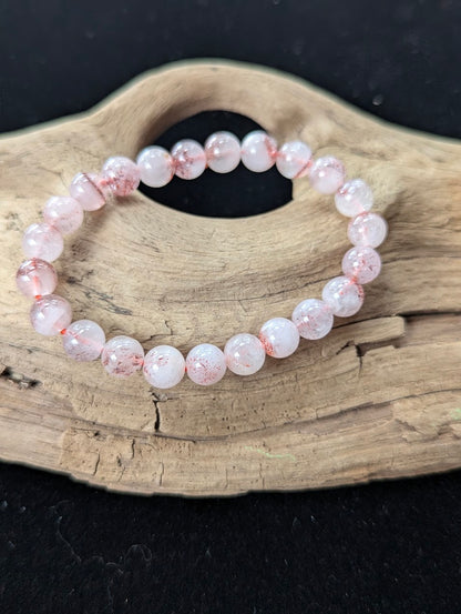 8mm AA Grade Super Seven gemstone bracelet resting on rustic wood, highlighting highly transparent quartz and red flecks.
