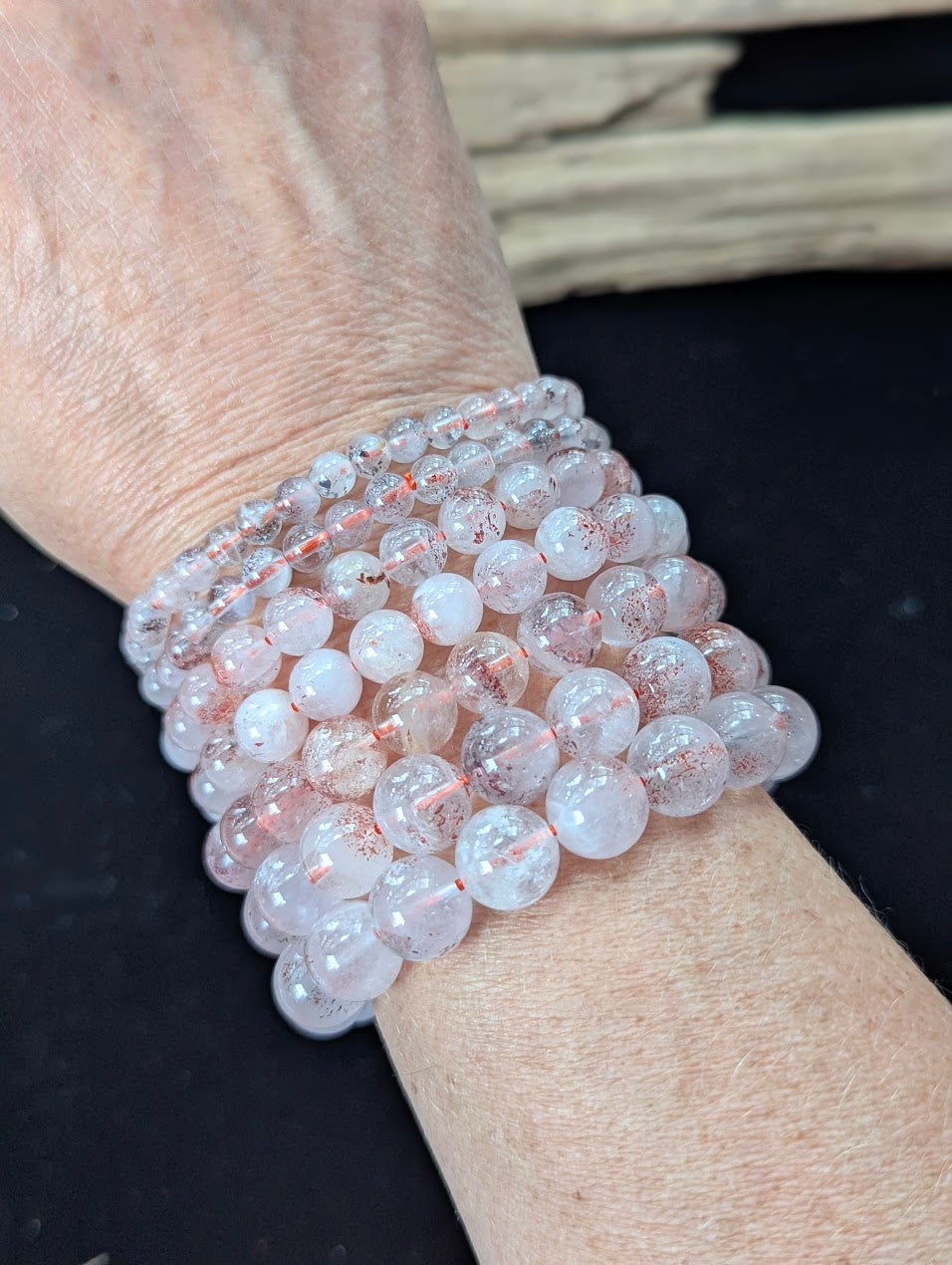 Multiple AA Grade Super Seven beaded bracelets stacked together on a wrist, demonstrating the high clarity and red inclusions across the different sizes.