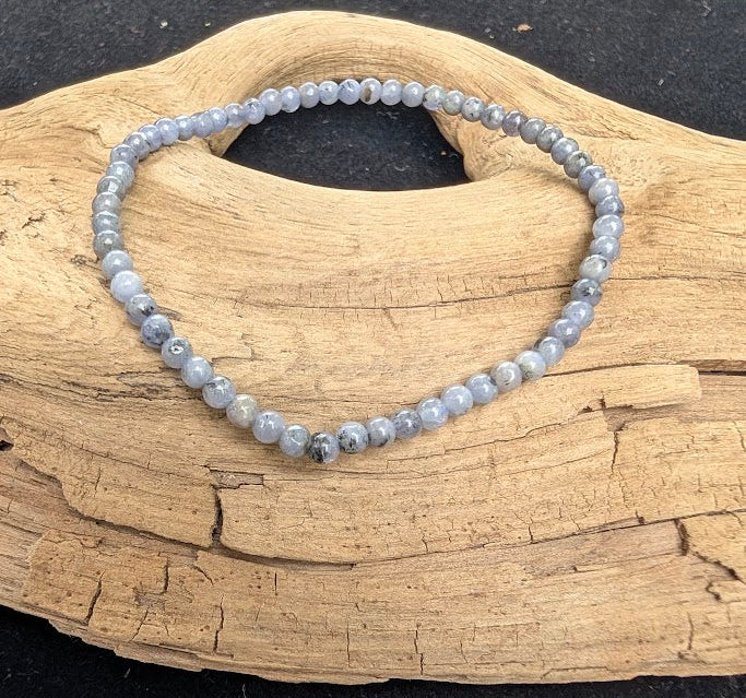 3mm polished Tanzanite beaded stretch bracelet resting on a driftwood display, showing pale periwinkle and grey-blue tones.