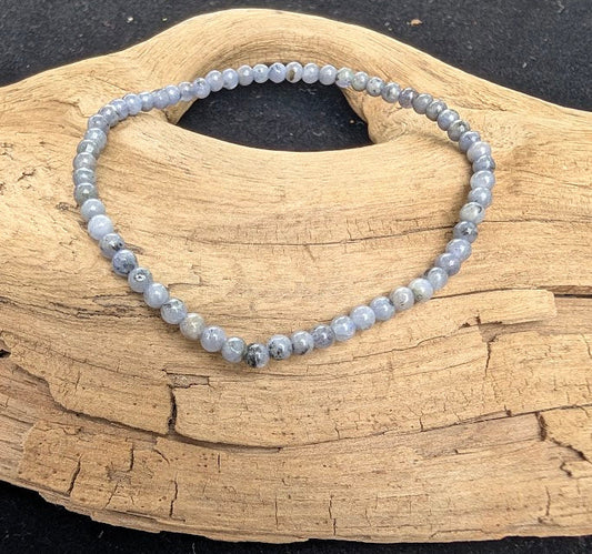 3mm polished Tanzanite beaded stretch bracelet resting on a driftwood display, showing pale periwinkle and grey-blue tones.