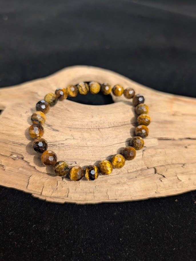 8mm faceted Tiger Eye beaded stretch bracelet resting on a driftwood display, showing golden chatoyancy.