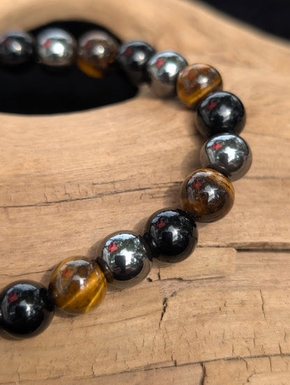 Macro view of polished 8mm Tiger Eye, Hematite, and Obsidian spherical beads on driftwood, highlighting the natural chatoyancy and metallic luster.