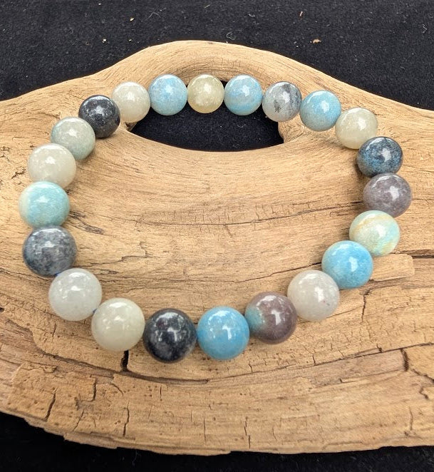 8mm polished Trolleite beaded stretch bracelet resting on a driftwood display, showing marbled blue, indigo, and white tones.