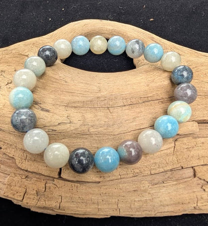 8mm polished Trolleite beaded stretch bracelet resting on a driftwood display, showing marbled blue, indigo, and white tones.
