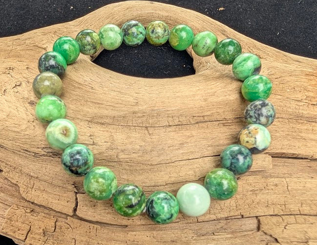 8mm polished Variscite beaded stretch bracelet resting on a driftwood display, showing mottled vibrant green tones and dark matrix webbing.