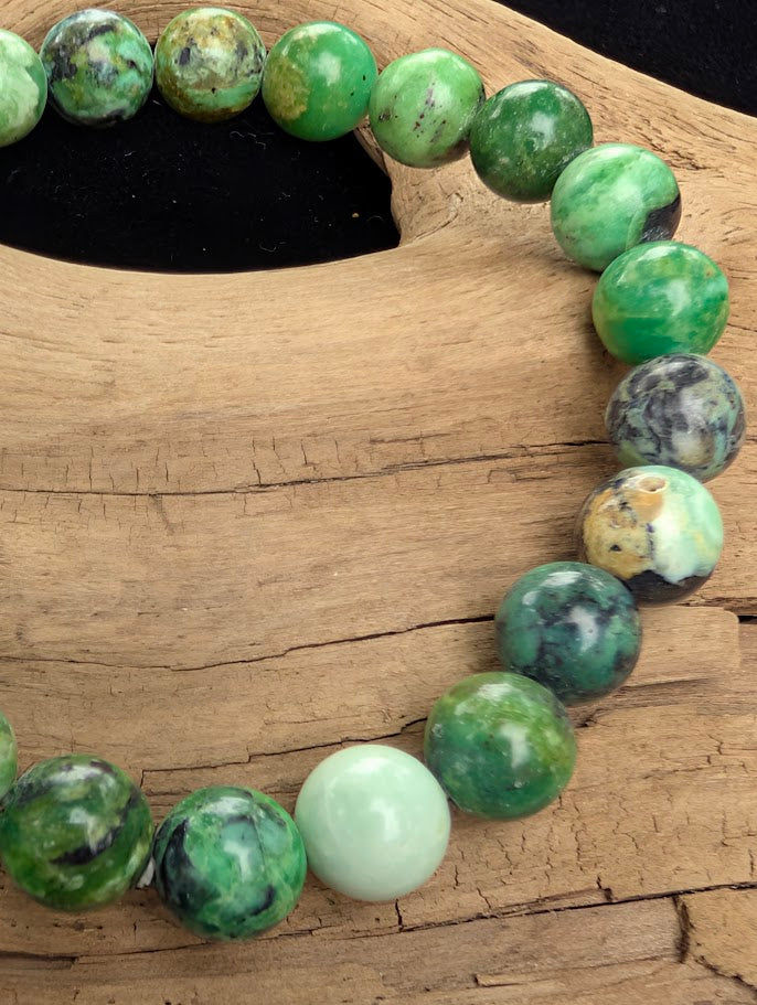Macro close-up of 8mm polished Variscite beads highlighting the high-gloss finish, apple-green colouration, and natural black and brown matrix.