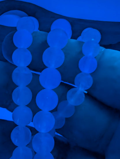 Handheld Velvet Fluorite bracelet glowing blue under UV light showing even transparency