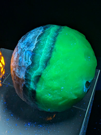 Volcano Agate carved moon sphere displaying intense orange fluorescence under UV illumination on an acrylic display stand.