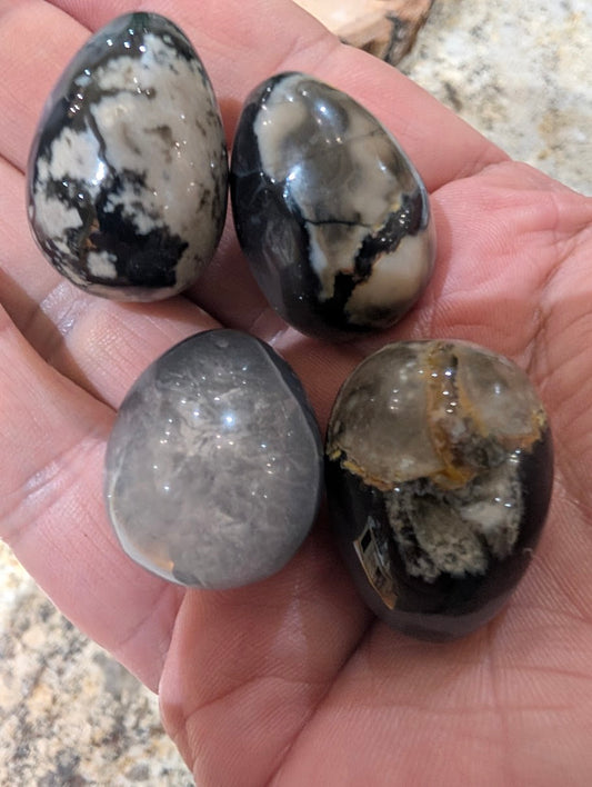 Four small Volcano Agate eggs held in a hand to show 1-inch scale and polished finish.