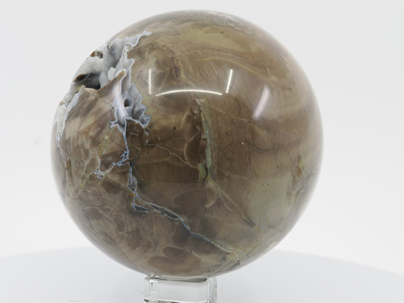 Side profile of a polished Volcano Agate sphere showing earthy brown and olive green banding and a small vug opening.