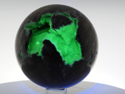 Volcano Agate sphere fluorescing intense neon green under 365nm UV light within its internal crystal cavity.