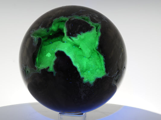 Volcano Agate sphere fluorescing intense neon green under 365nm UV light within its internal crystal cavity.