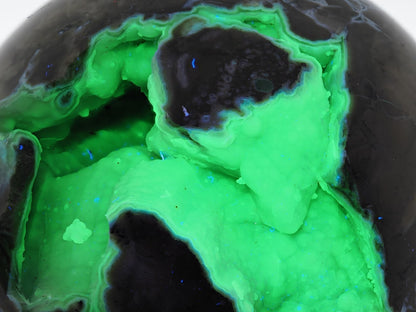 Detailed shot of reactive chalcedony crystals glowing bright green under ultraviolet light inside an agate sphere.