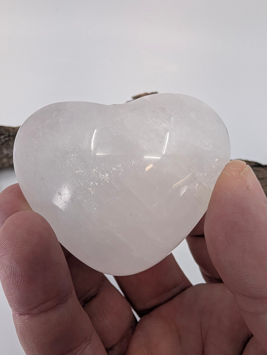 Hand holding a 100g White Calcite heart showing soft white color.