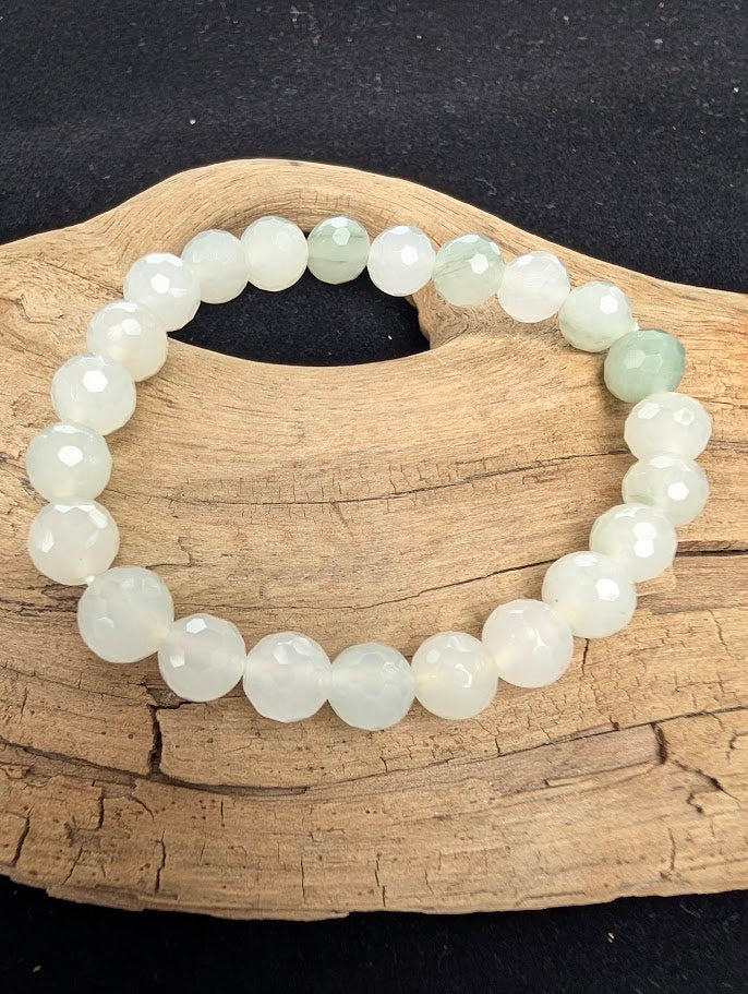 8mm faceted White Jade beaded stretch bracelet resting on a driftwood display, showing milky-white and pale green translucency.