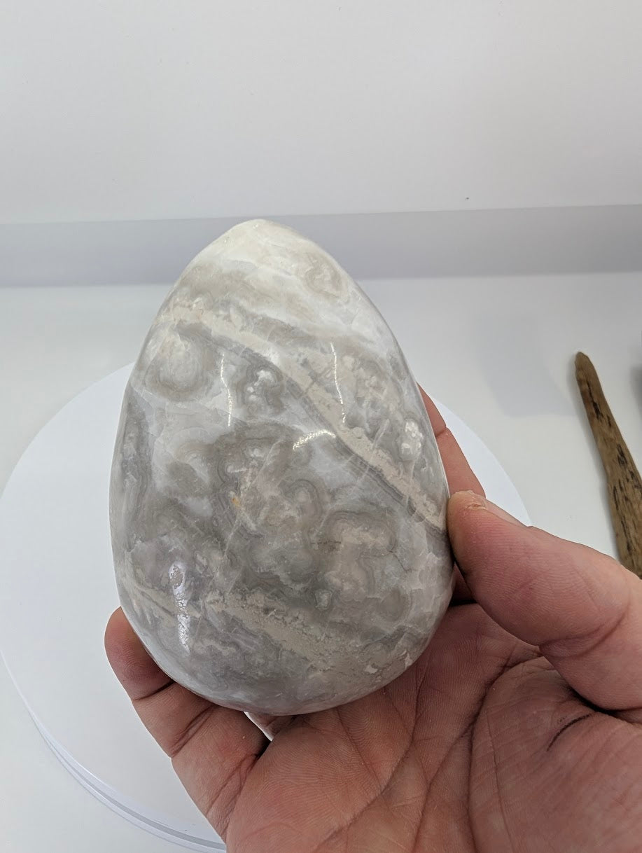 Hand-held white Mexican lace agate egg showing scale and polish