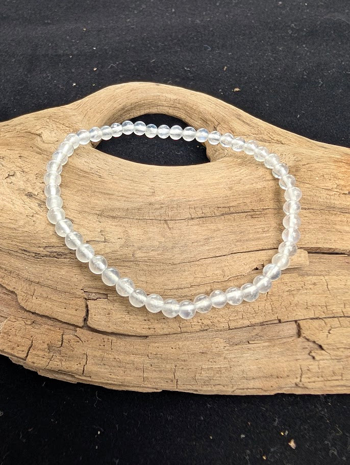 4mm polished White Moonstone beaded stretch bracelet resting on a driftwood display, showing milky translucency and subtle adularescent flash.