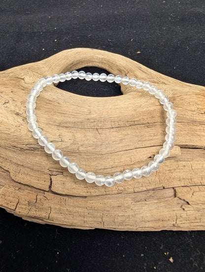 4mm polished White Moonstone beaded stretch bracelet resting on a driftwood display, showing milky translucency and subtle adularescent flash.