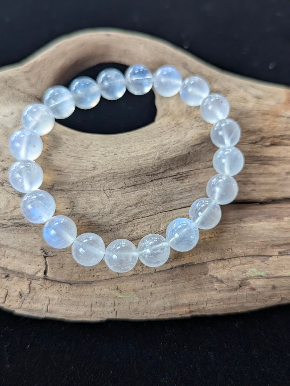 Substantial 10mm AAA Grade White Moonstone gemstone bracelet resting on rustic wood, highlighting luminous blue flash.