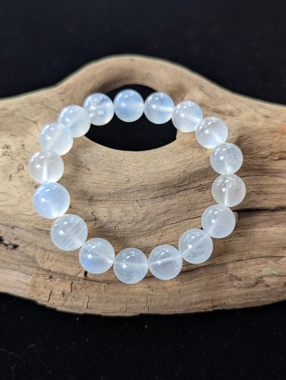 11mm AAA Grade White Moonstone statement bracelet resting on textured driftwood.
