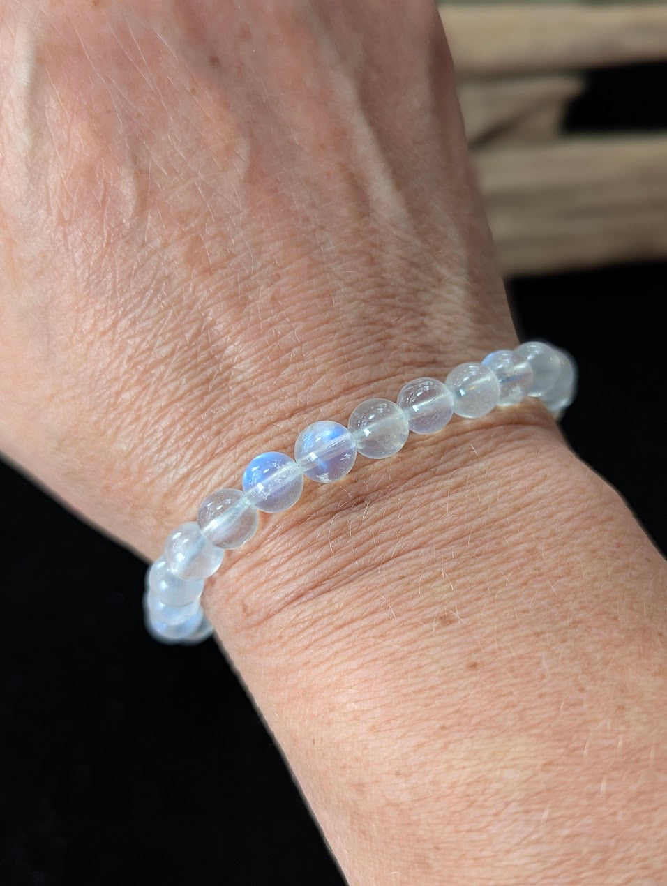 7mm White Moonstone beaded bracelet worn on a wrist, demonstrating the luminous blue flash catching the light.