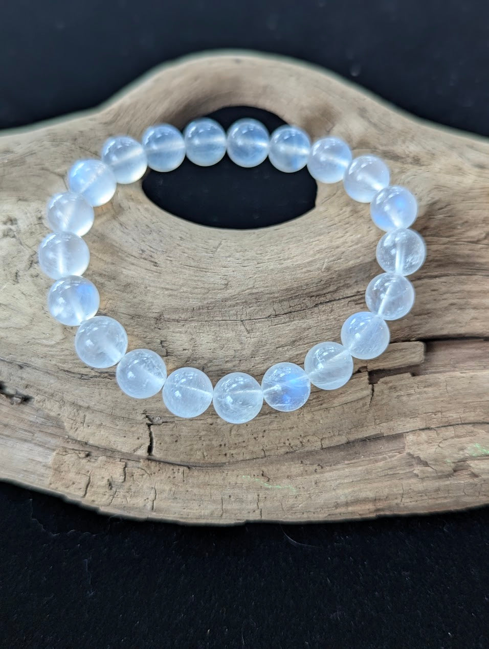 9mm High Quality Sri Lankan White Moonstone bracelet displayed on natural driftwood, showing glassy bead clarity and blue sheen.