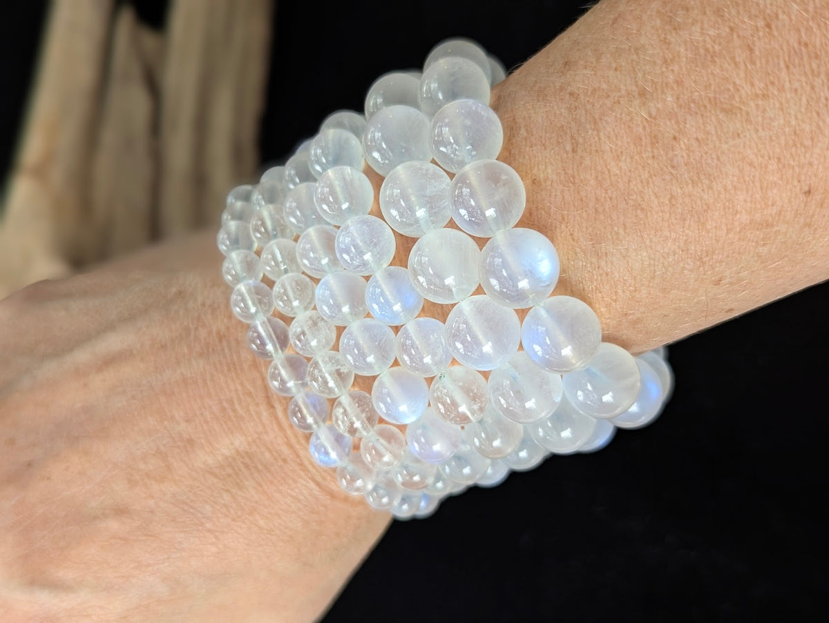 Multiple AAA Grade White Moonstone beaded bracelets stacked together on a wrist, demonstrating the high clarity and blue flash across the different bead sizes.