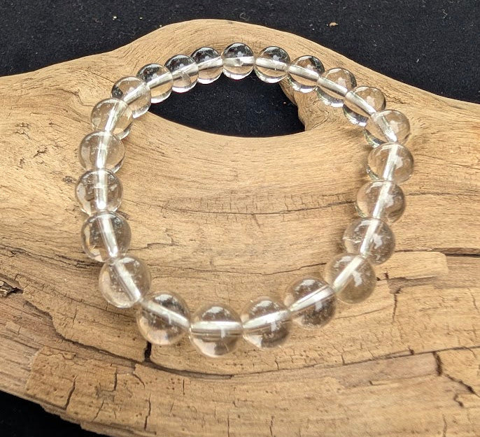 8mm AA-grade polished White Topaz beaded stretch bracelet from Sri Lanka resting on a driftwood display, showing exceptional water-clear transparency.