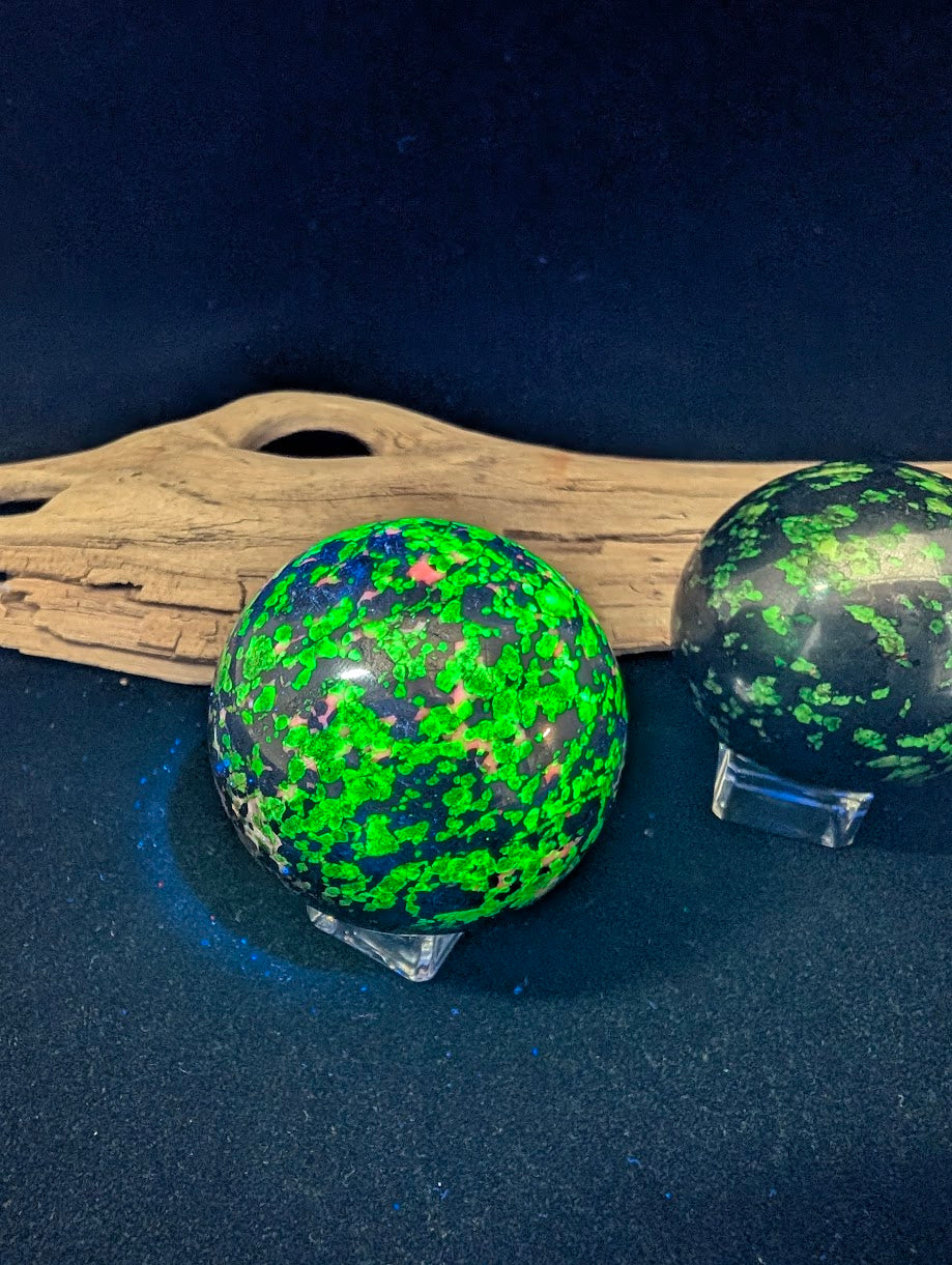 Two fluorescent spheres under shortwave UV light showing neon green willemite versus blue hydrozincite reaction.