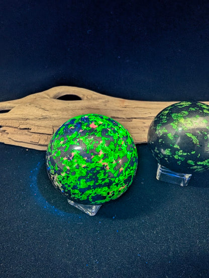 Two fluorescent spheres under shortwave UV light showing neon green willemite versus blue hydrozincite reaction.