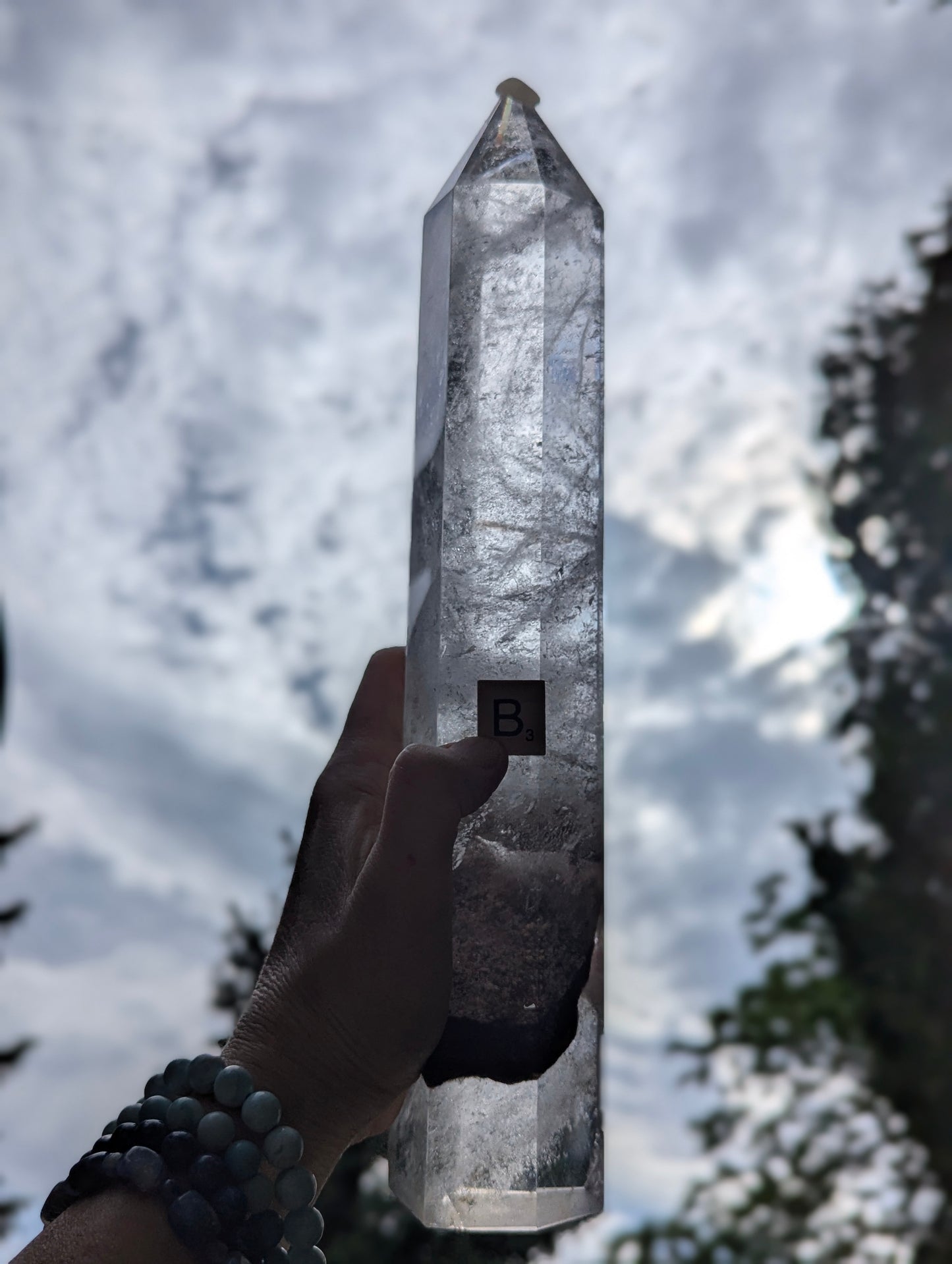 Backlit Garden Quartz Tower B held against the sky showing translucent quartz, internal veils, and garden inclusions