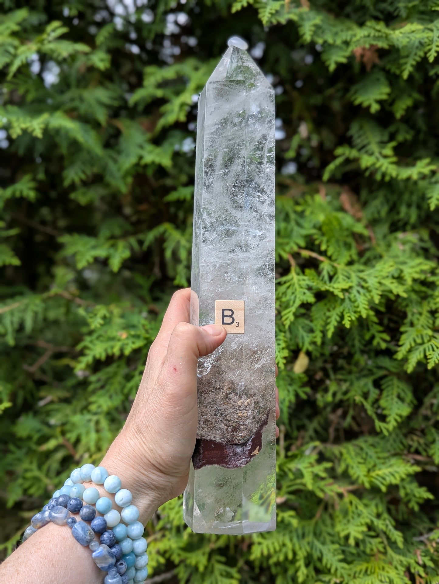 Large Garden Quartz Tower B held outdoors for scale with earthy lower inclusion and misty internal quartz veils