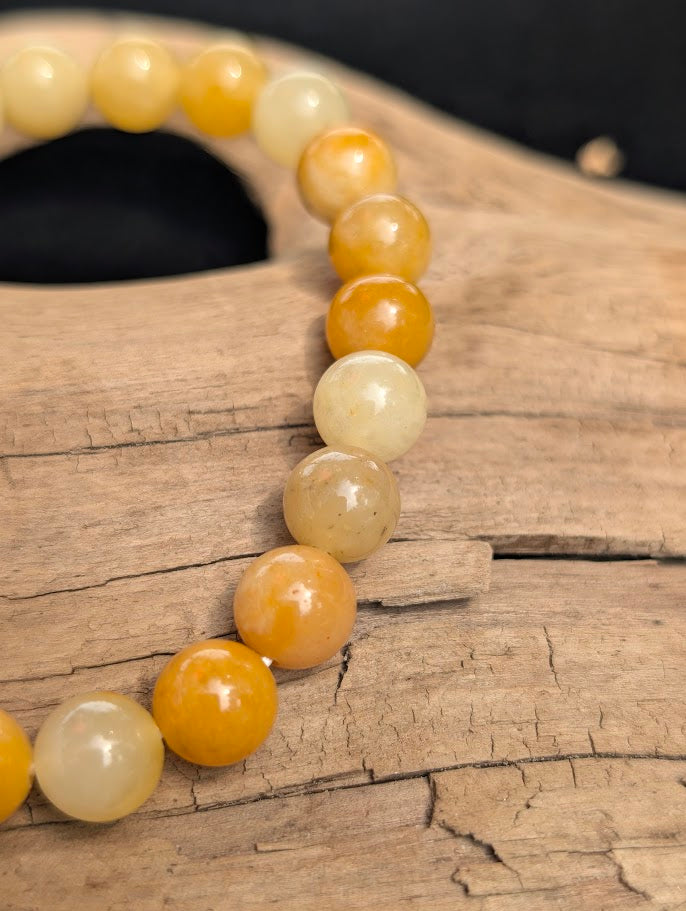 Macro view of polished 8mm Yellow Aventurine spherical beads on driftwood, highlighting natural colour zoning and subtle internal quartz structures.