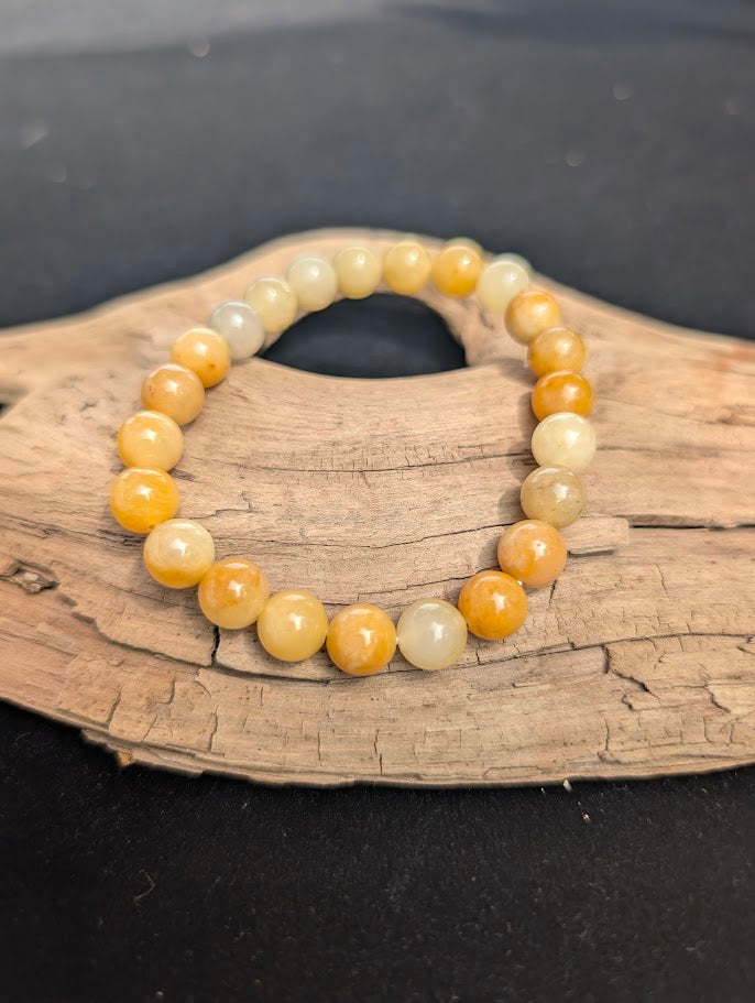 An 8mm Yellow Aventurine beaded bracelet resting on natural driftwood, displaying translucent pale yellow to rich golden-orange colours.