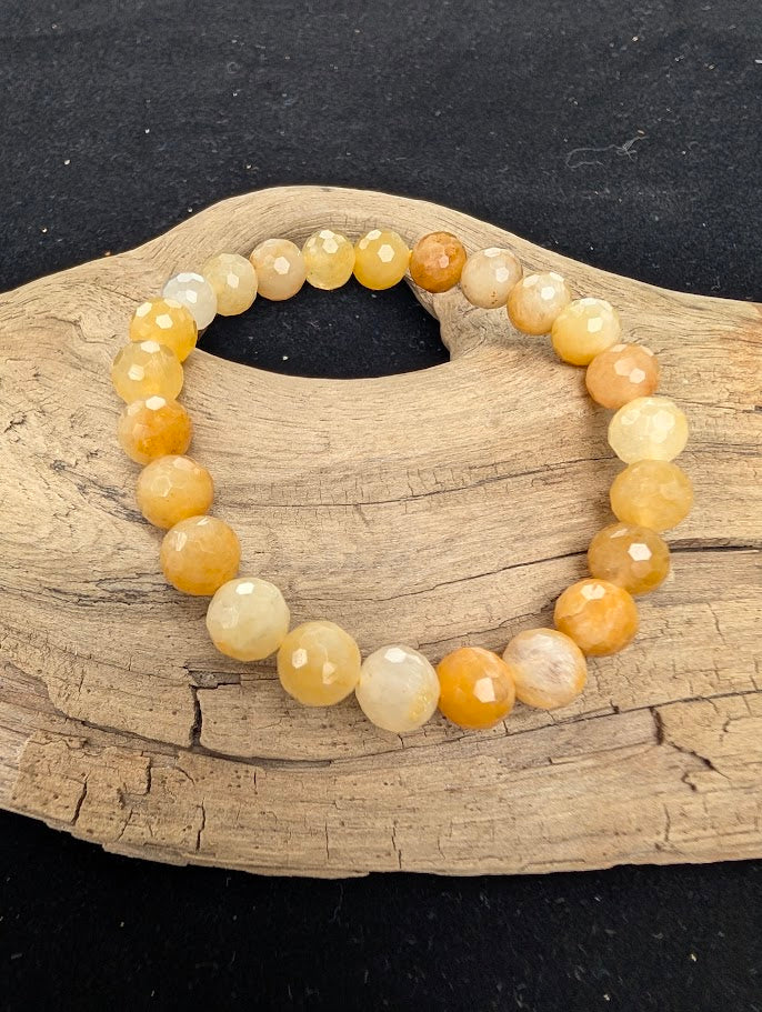 8mm faceted Yellow Aventurine beaded stretch bracelet resting on a driftwood display, showing bright yellow and golden tones.