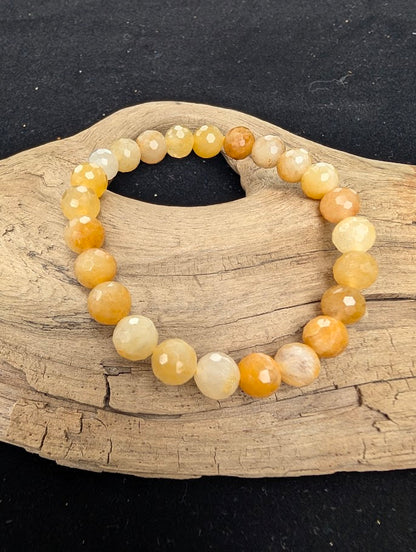 8mm faceted Yellow Aventurine beaded stretch bracelet resting on a driftwood display, showing bright yellow and golden tones.