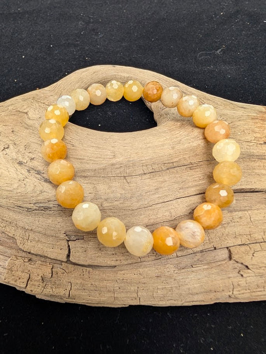 8mm faceted Yellow Aventurine beaded stretch bracelet resting on a driftwood display, showing bright yellow and golden tones.