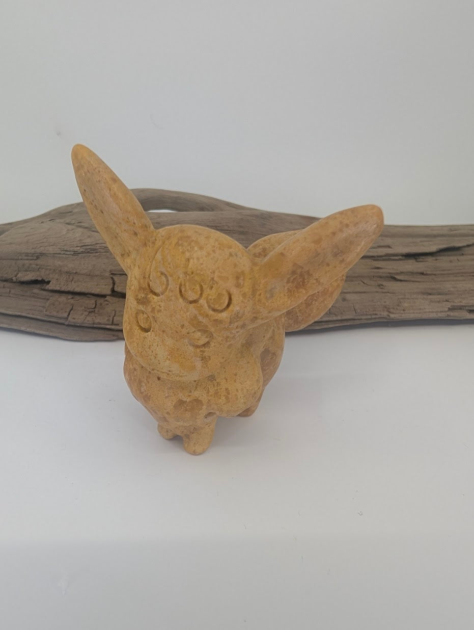 Front view of a 70mm hand-carved Eevee figurine made from natural yellow jade with a smooth waxy finish and mustard-yellow tones.