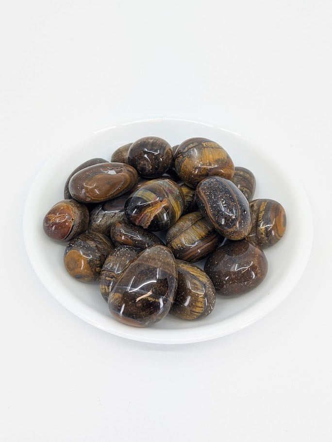 Yellow Tiger Eye tumbled stones in white dish showing chatoyant golden shimmer