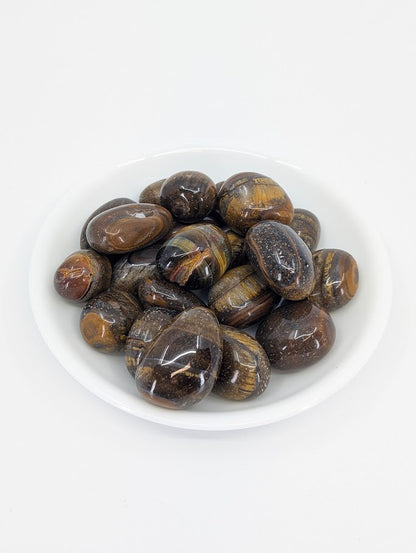 Yellow Tiger Eye tumbled stones in white dish showing chatoyant golden shimmer